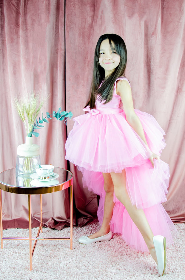 Asymmetrical high-low hem girl princess dress in bright pink with a multi-layer tulle skirt, satin top, open back and a pink bow.