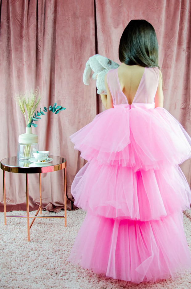 Asymmetrical high-low hem girl princess dress in bright pink with a multi-layer tulle skirt, satin top, open back and a pink bow.