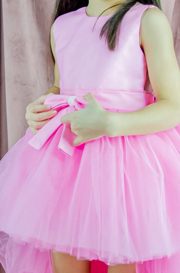 Asymmetrical high-low hem girl princess dress in bright pink with a multi-layer tulle skirt, satin top, open back and a pink bow.