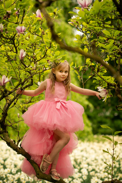 Asymmetrical high-low hem girl princess dress in bright pink with a multi-layer tulle skirt, satin top, open back and a pink bow.