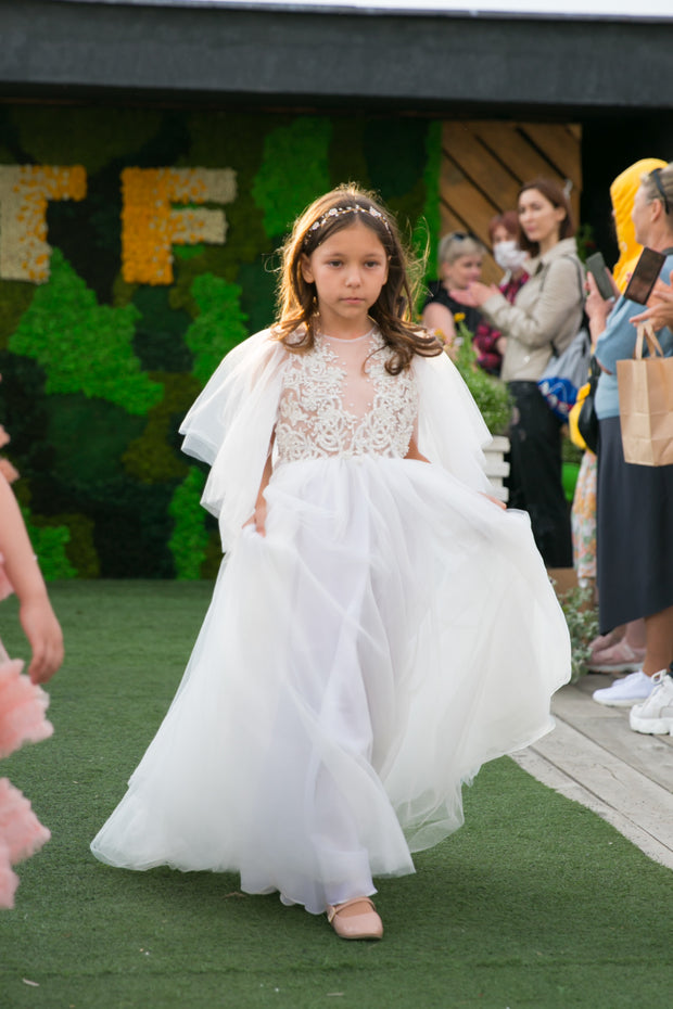 Floor-length white tulle princess dress with a floating tulle skirt, transparent butterfly sleeves and transparent bodice covered with embellished flower details and pearls. Girl dress for flower girls, weddings, communion or birthday party.