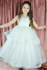 Long, white A-line flower girl dress with an asymmetrical multi-layer tulle skirt and white satin top with pleated satin details.