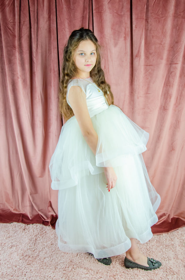 Long, white A-line flower girl dress with an asymmetrical multi-layer tulle skirt and white satin top with pleated satin details.