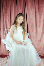 Long, white A-line flower girl dress with an asymmetrical multi-layer tulle skirt and white satin top with pleated satin details.