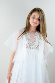 Floor-length white tulle princess dress with a floating tulle skirt, transparent butterfly sleeves and transparent bodice covered with embellished flower details and pearls. Girl dress for flower girls, weddings, communion or birthday party.