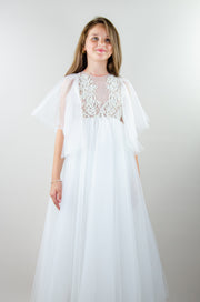 Floor-length white tulle princess dress with a floating tulle skirt, transparent butterfly sleeves and transparent bodice covered with embellished flower details and pearls. Girl dress for flower girls, weddings, communion or birthday party.