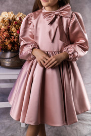 Knee-length satin girl dress in a blush pink colour. The dress features an a-line satin skirt with tulle underskirt which gives it volume. Satin top with high neckline is accentuated with a cute bow and long satin sleeves. For special occasions: Wedding, Birthday party, Prom, Flower girl, Eid and other events.