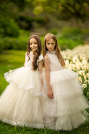 Long, white A-line flower girl dress with an asymmetrical multi-layer tulle skirt and white satin top with pleated satin details.